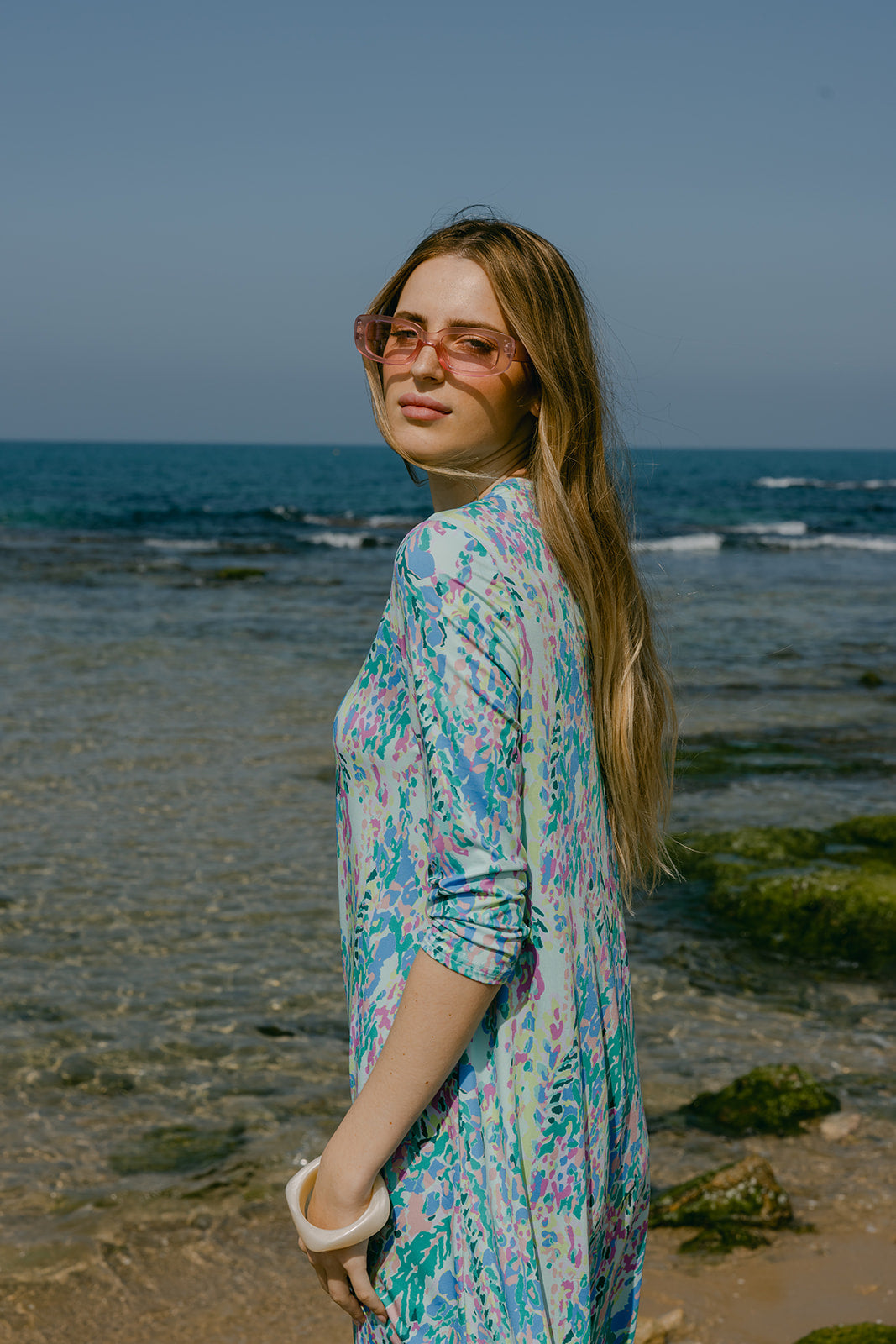 Woman in a floral dress standing on a beach with ocean in the background